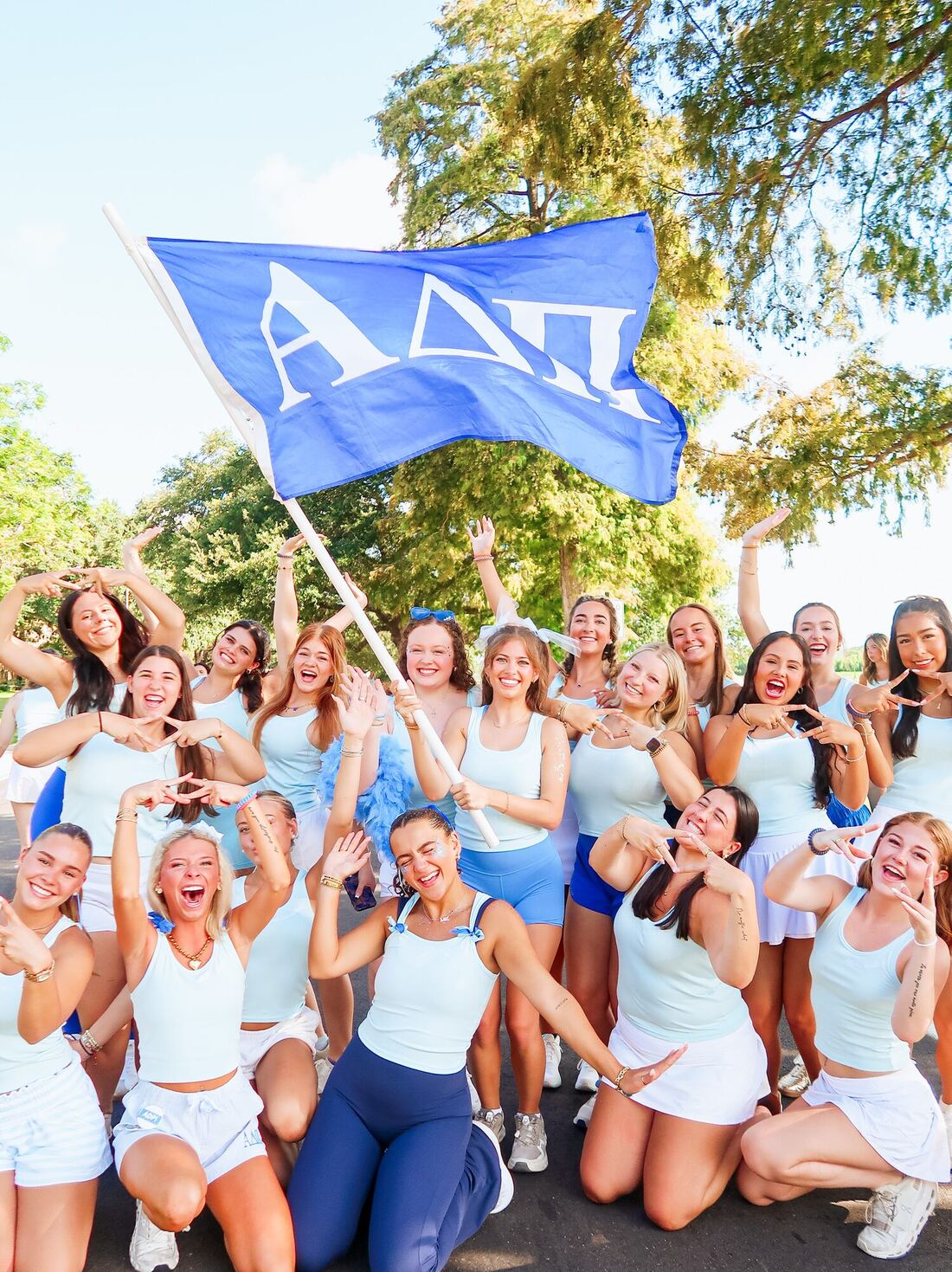 Alpha Delta Pi members in light blue cheering under a blue ΑΔΠ flag