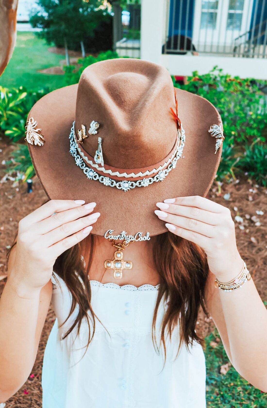 A cowboy hat decorated with jewelry pins and a “Country's Cool” necklace, held up in front of the chapter house